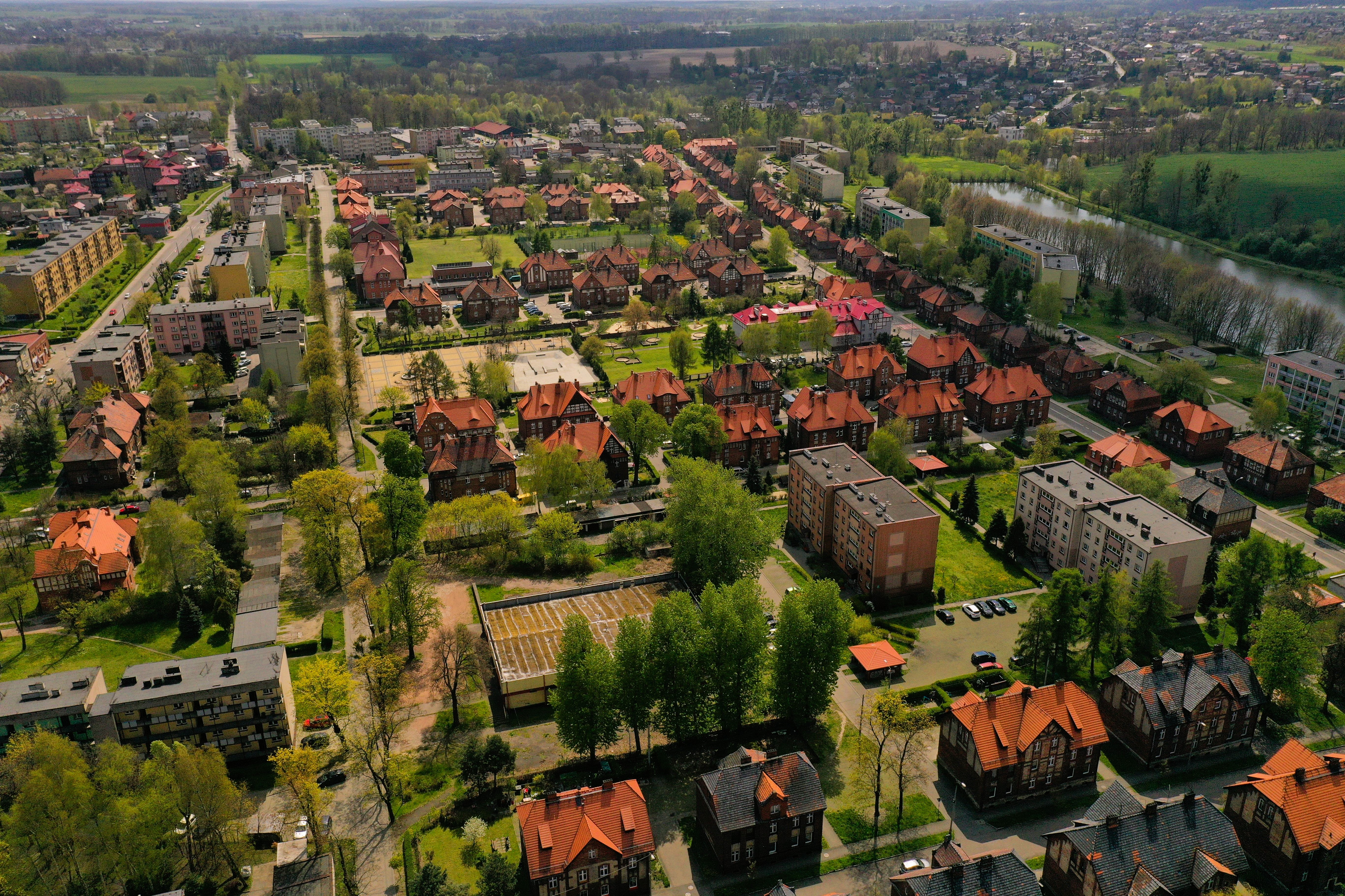 Widok w góry na zabudowę mieszkaniową, bloki i kamienice z pomarańczowymi dachami, rozdzieloną terenami zielonymi i drzewami, z prawej strony dolina rzeczna.