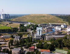 Widok w góry na rozproszoną zabudowę zakładu przemysłowego, w tle hałda i kilka szerokich kominów elektrociepłowni.