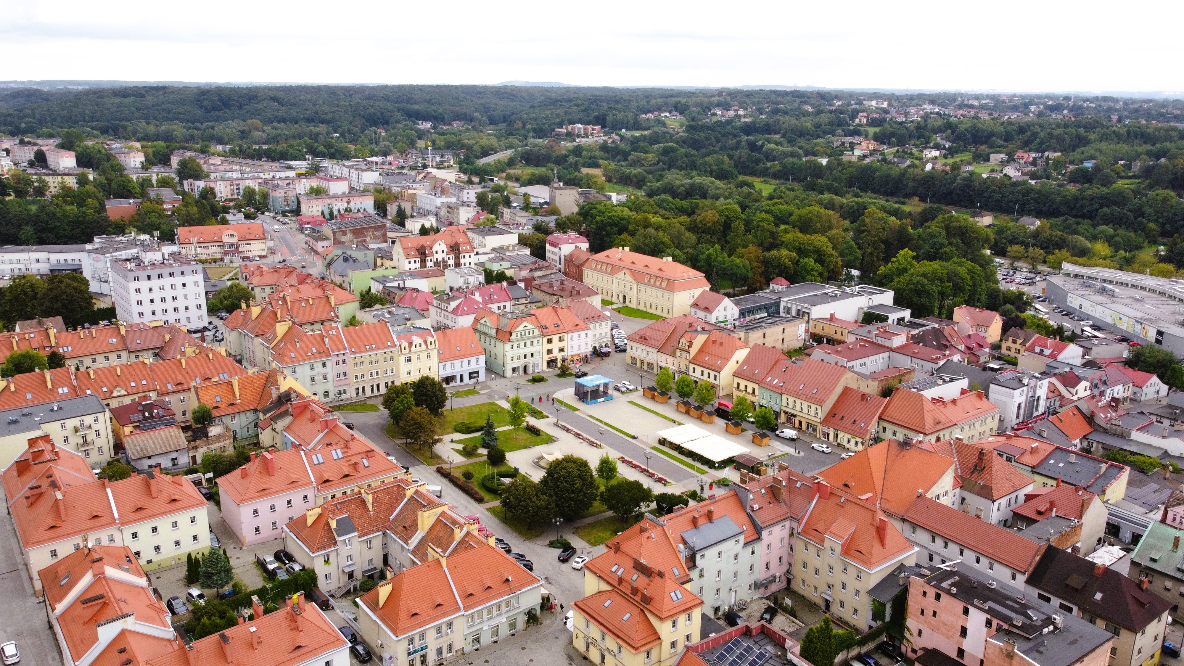 Widok z góry na zabudowę miejską z zachowanym układem historycznym, w tle tereny parkowe, lasy i zarysy innej zabudowy.
