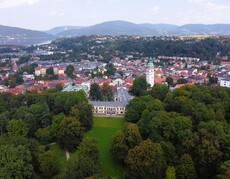 Widok w góry na zespół pałacowo-parkowo-klasztorny, zabudowa historyczna, w tle szczyty górskie.